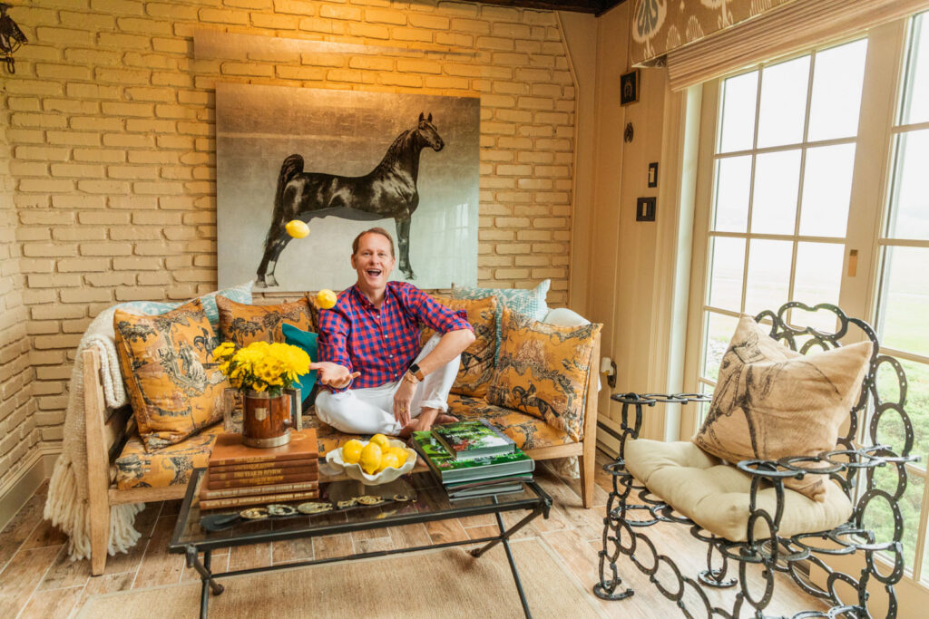 Carson Kressley seated on a sofa beneath a horse painting at his home