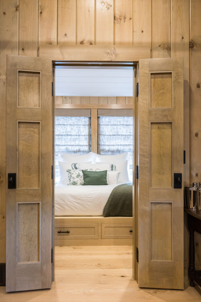 Paneled wood double doors opening onto a bedroom with white bedding and green accents