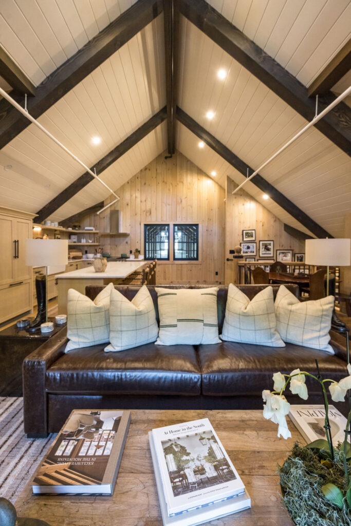 Vaulted living space with exposed dark beams, a leather sofa and the kitchen beyond