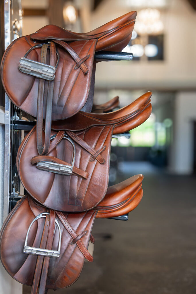 Three brown leather saddles on wall-mounted racks in the barn