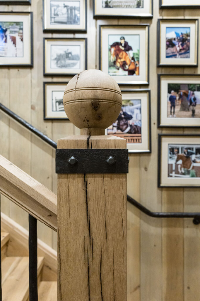 Rustic wood stair newel post in front of a gallery wall of framed equestrian competition photos