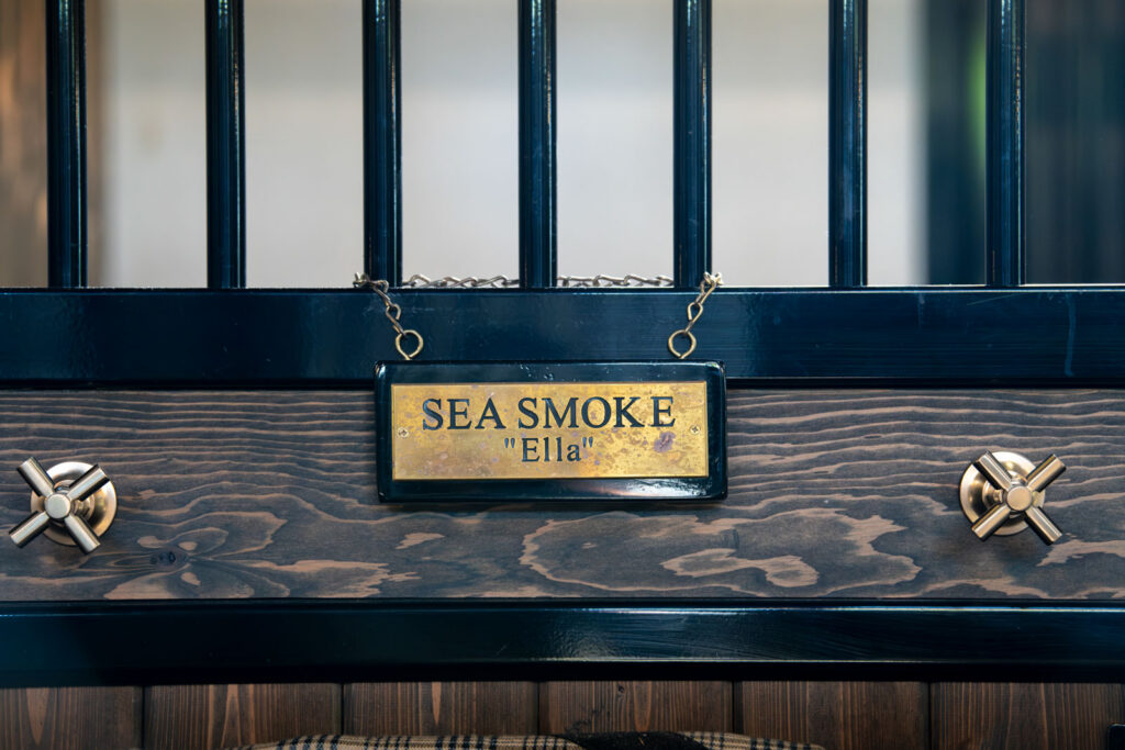 Brass stall nameplate reading Sea Smoke “Ella” on a black stall front