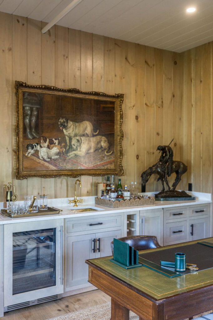 Wood-paneled lounge with a wet bar, beverage refrigerator, leather-topped desk and an oil painting of hounds