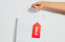 person holding a white paper bag with sale card