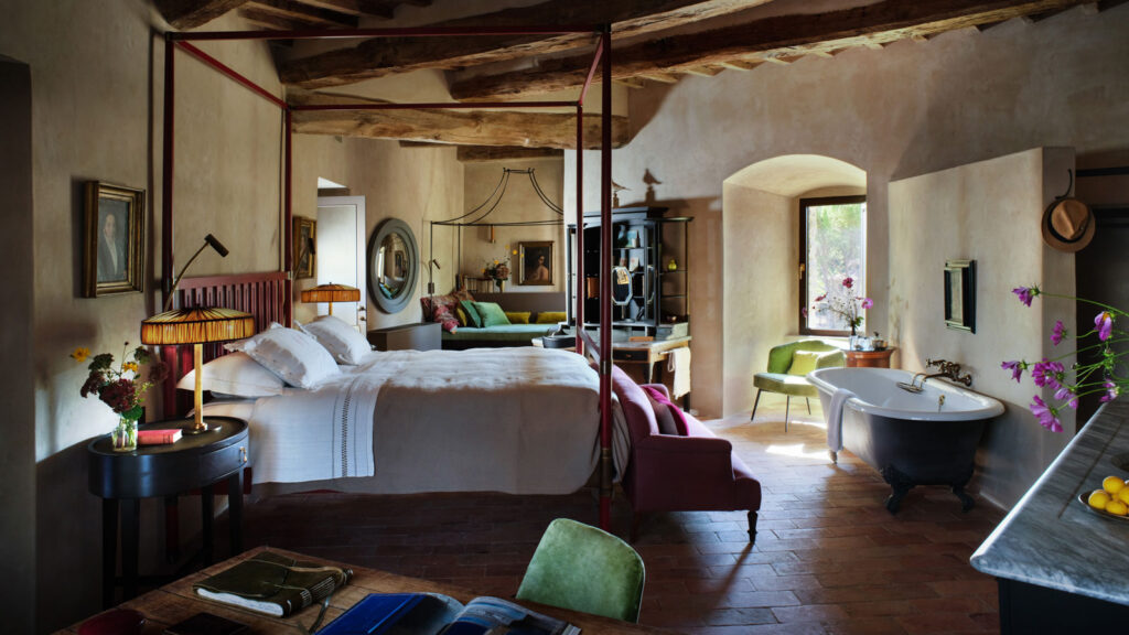A four-poster bedroom suite at Castello di Reschio with exposed wood beams and a freestanding clawfoot bathtub