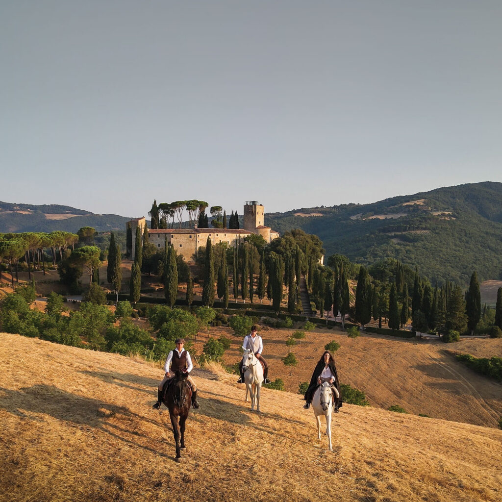 Riders on horseback approaching Castello di Reschio through the Umbrian countryside at sunset