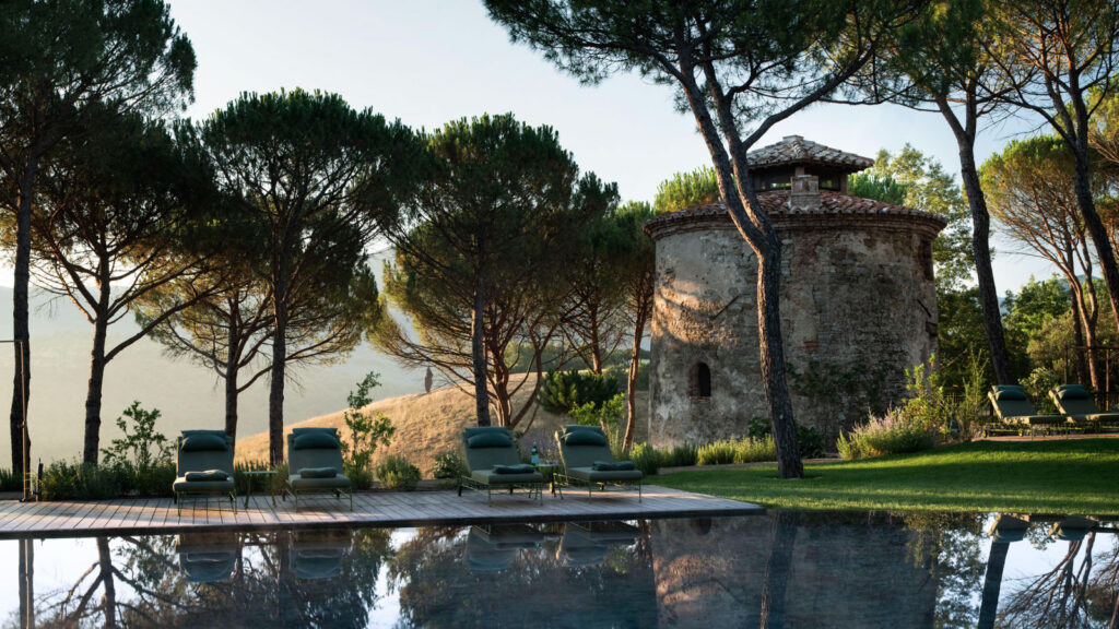 The reflecting pool at Castello di Reschio at golden hour with the ancient stone tower and pine trees