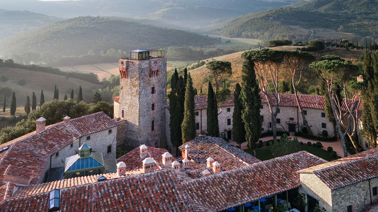 Aerial view of Castello di Reschio's medieval tower and stone buildings surrounded by cypress trees in the Umbrian hills