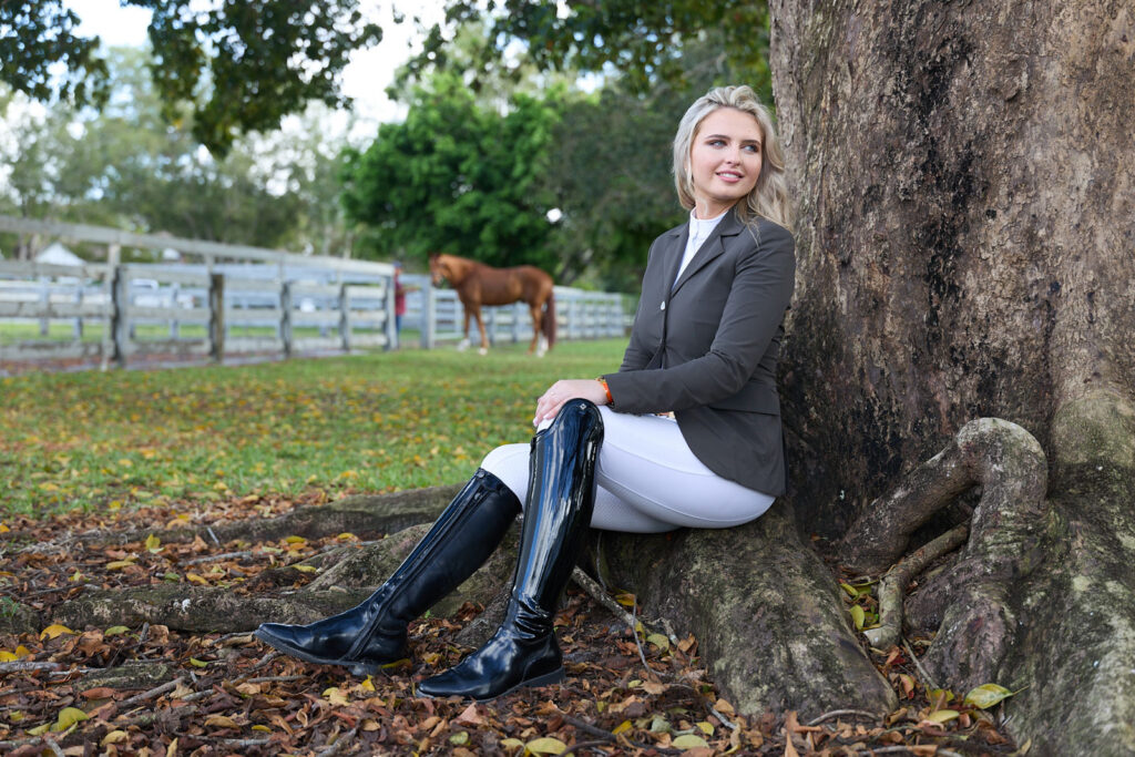 Kat Fuqua sits under a tree with one of her horses grazing nearby