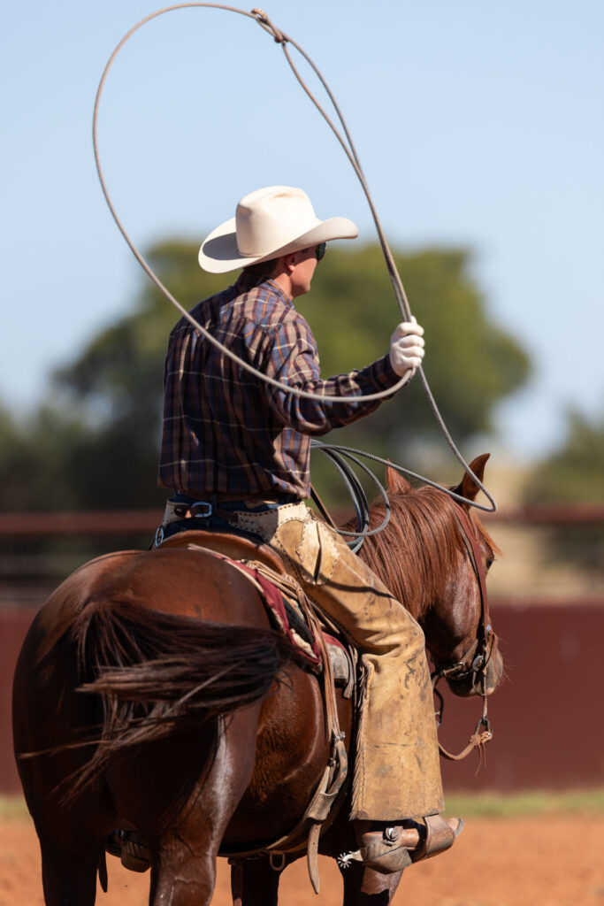 A Four Sixes cowboy swinging a rope on horseback