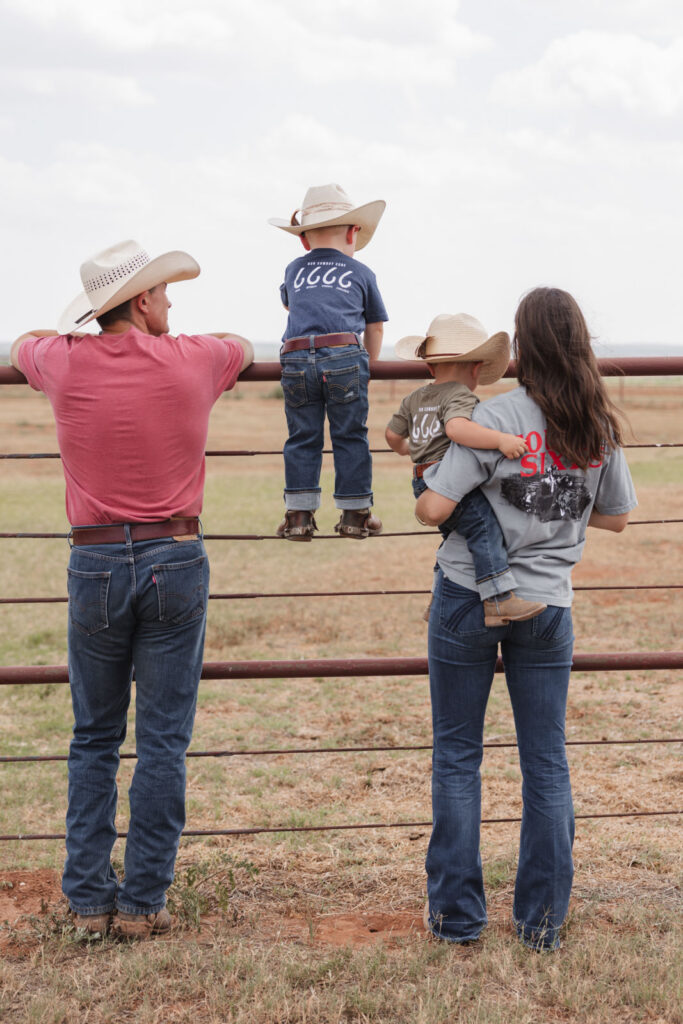 A family in cowboy hats watching from a fence at the Four Sixes Ranch